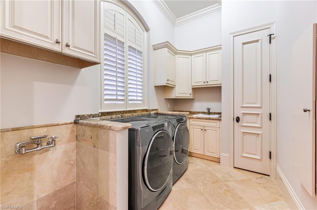 Laundry room featuring washing machine and clothes dryer, crown molding, sink, and cabinets