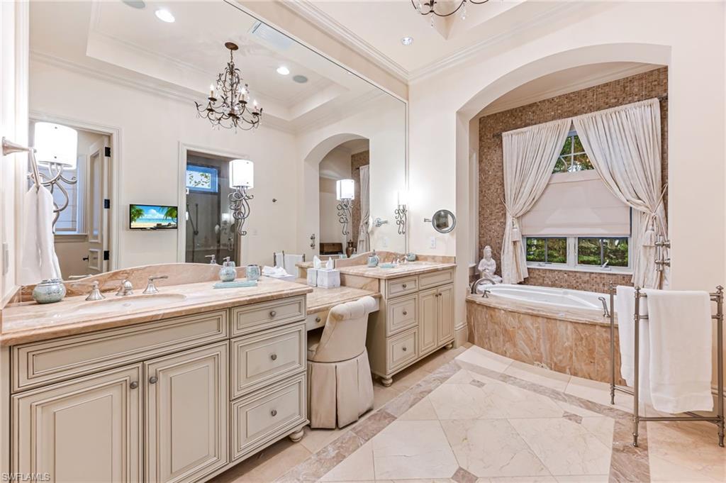Bathroom with vanity, a raised ceiling, crown molding, a relaxing tiled tub, and a chandelier