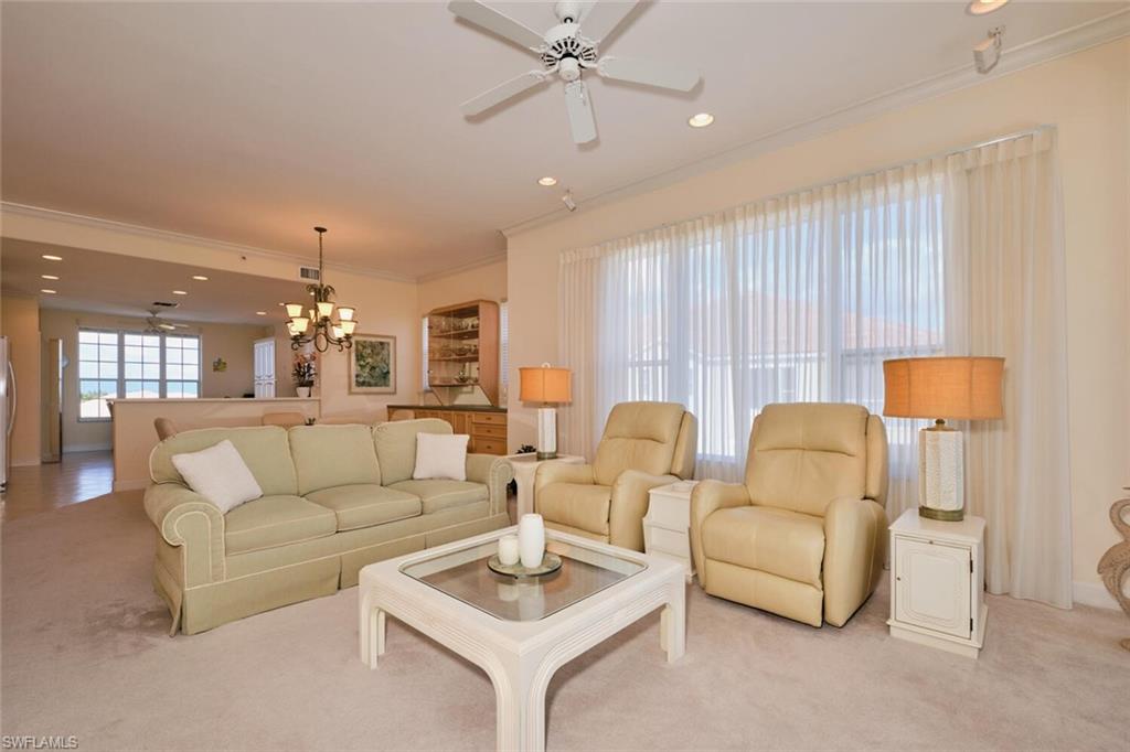 Living room with ceiling fan with notable chandelier, light carpet, and crown molding