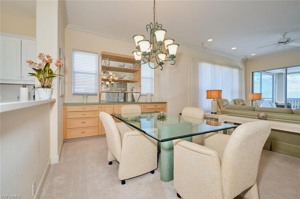 Carpeted dining room with ceiling fan with notable chandelier and crown molding