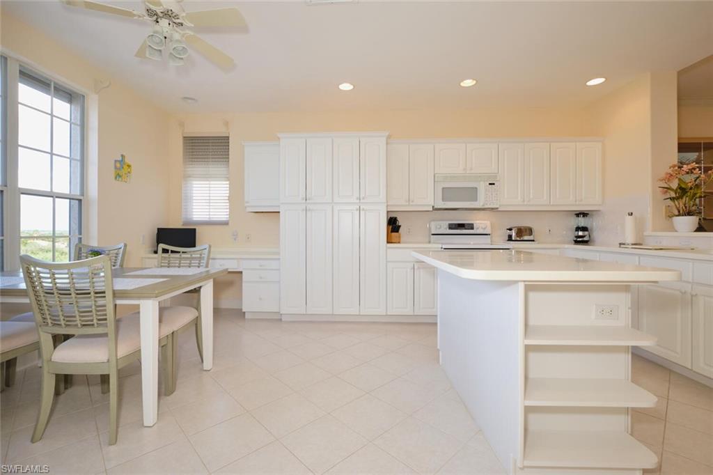 Kitchen with white appliances, ceiling fan, white cabinetry, and a center island