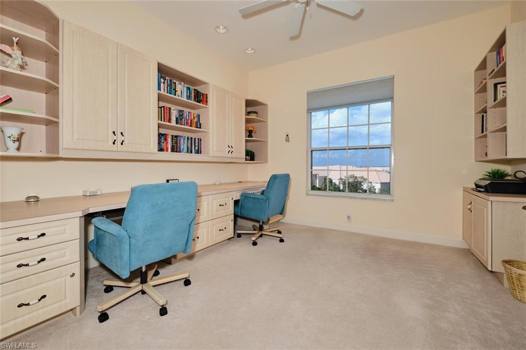 Carpeted office space with built in desk and ceiling fan