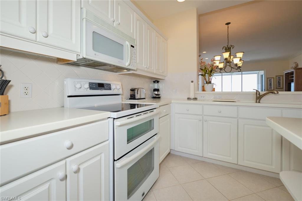 Kitchen featuring an inviting chandelier, white cabinets, light tile patterned floors, backsplash, and white appliances