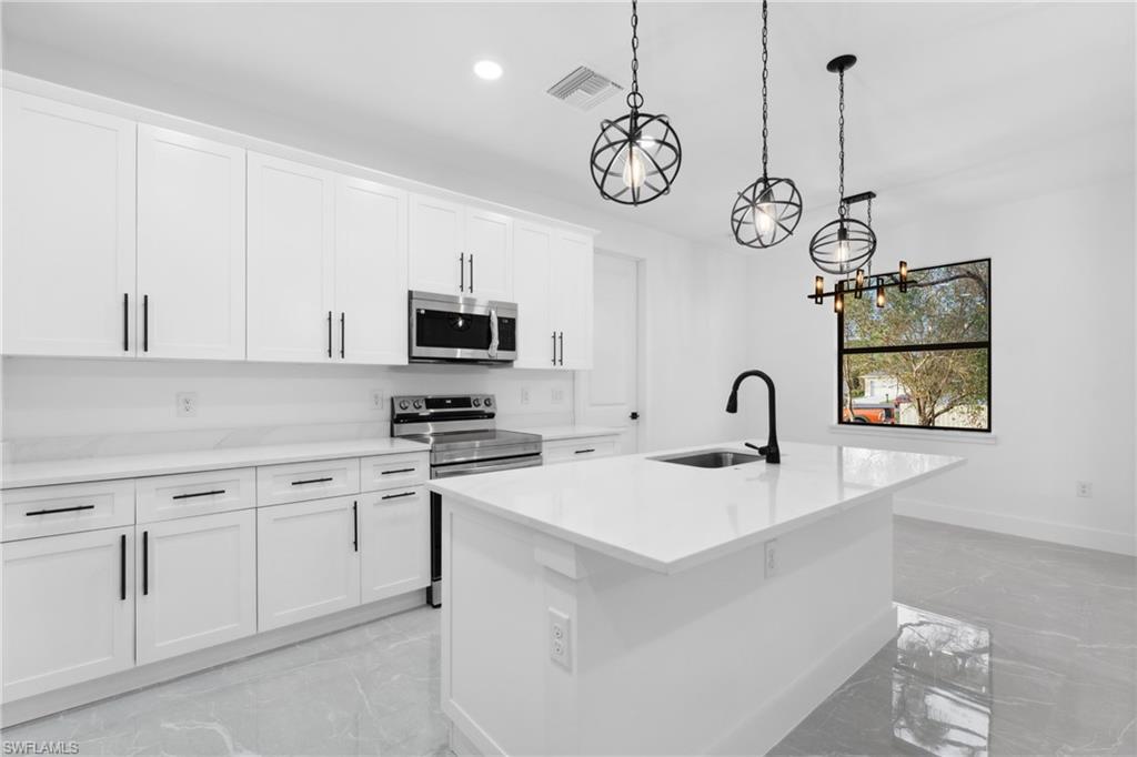 Kitchen with white cabinets, sink, hanging light fixtures, an island with sink, and stainless steel appliances