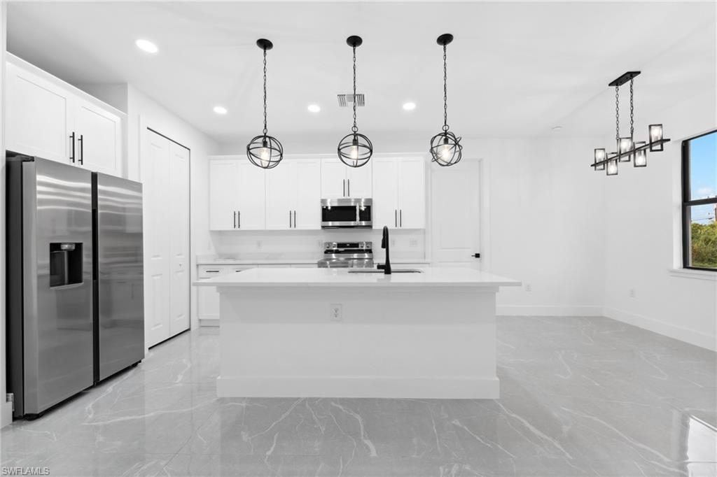Kitchen with a center island with sink, white cabinets, hanging light fixtures, and appliances with stainless steel finishes