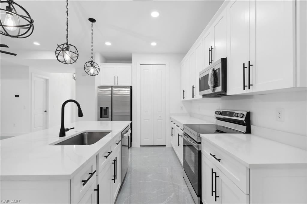 Kitchen featuring a center island with sink, sink, decorative light fixtures, white cabinetry, and stainless steel appliances