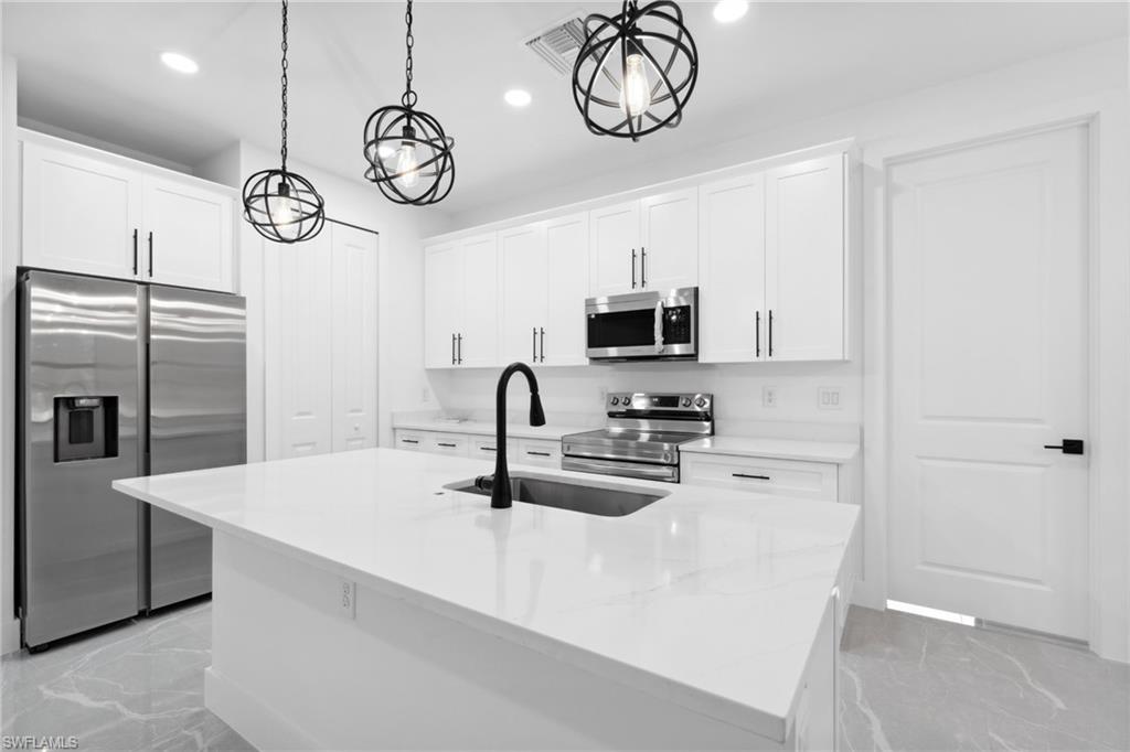 Kitchen with white cabinetry, a center island with sink, stainless steel appliances, and decorative light fixtures