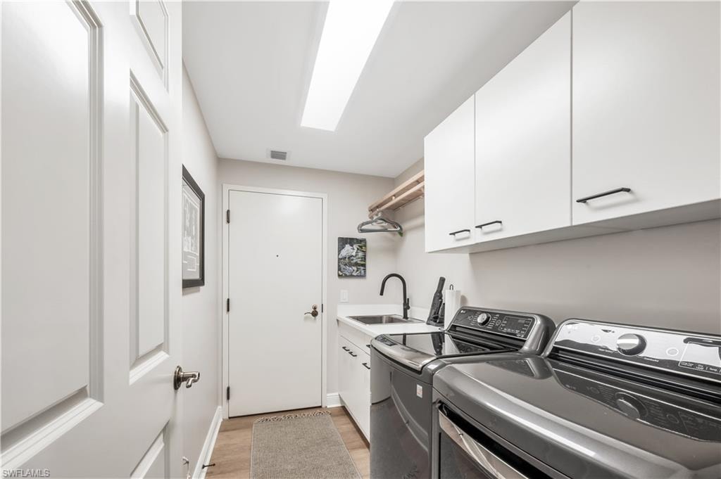 Washroom with cabinets, light wood-type flooring, sink, and washing machine and clothes dryer