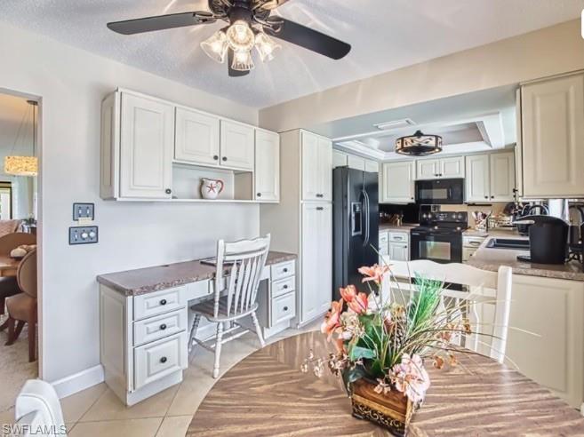 Kitchen with black appliances, a ceiling fan, white cabinetry, a raised ceiling, and light tile patterned floors