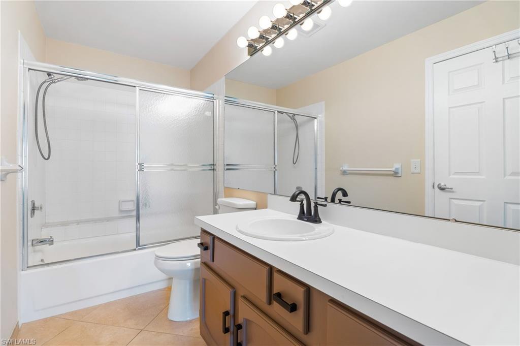 Full bathroom with tile patterned floors, vanity, bath / shower combo with glass door, and toilet