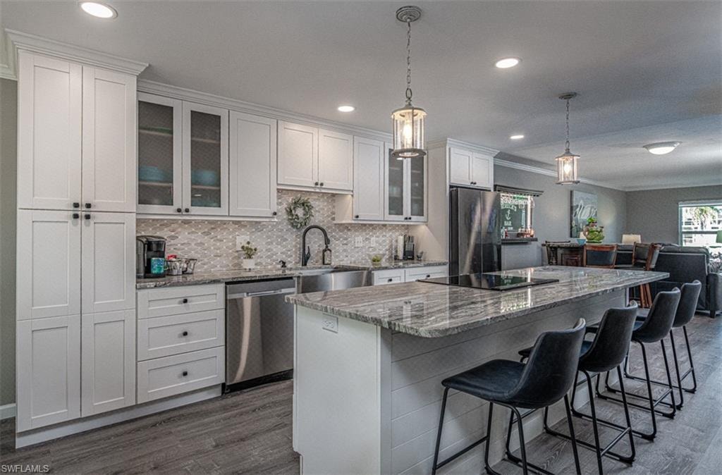 Kitchen featuring a center island, dark wood-type flooring, white cabinets, appliances with stainless steel finishes, and decorative light fixtures
