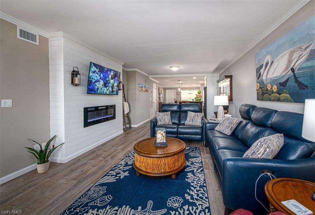 Living room with a large fireplace, wood-type flooring, and crown molding