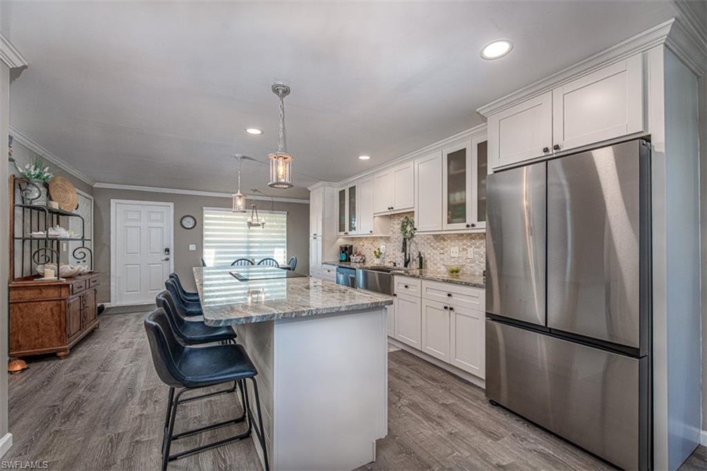 Kitchen with light stone countertops, white cabinetry, stainless steel appliances, and light wood-type flooring