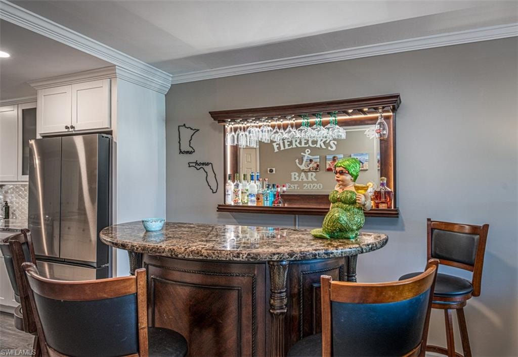 Bar featuring decorative backsplash, stainless steel fridge, dark stone counters, crown molding, and white cabinetry