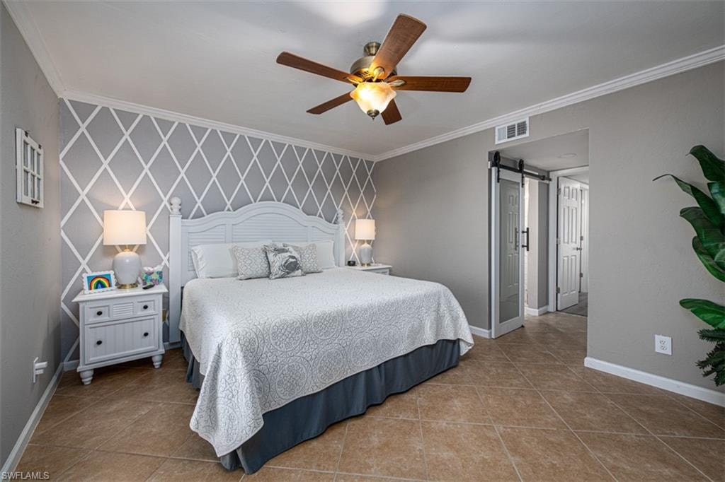 Tiled bedroom with ceiling fan, a barn door, and crown molding