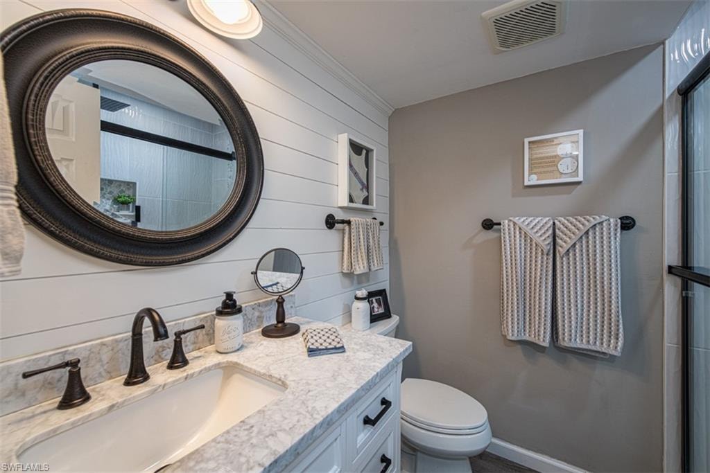 Bathroom featuring ornamental molding, vanity, a shower with door, toilet, and wood walls
