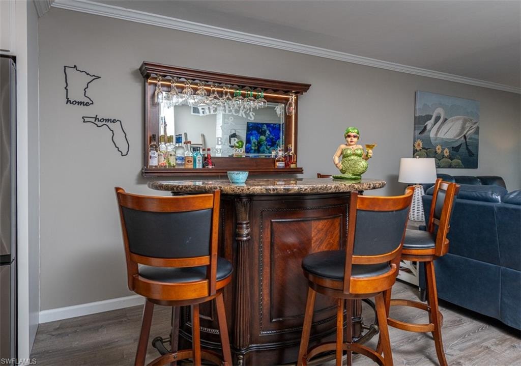 Bar featuring hardwood / wood-style floors, stainless steel refrigerator, and ornamental molding