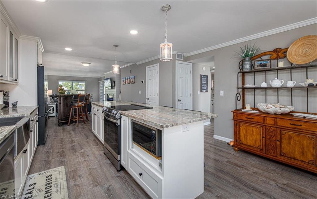 Kitchen featuring a center island, dark hardwood / wood-style floors, light stone counters, white cabinetry, and stainless steel appliances