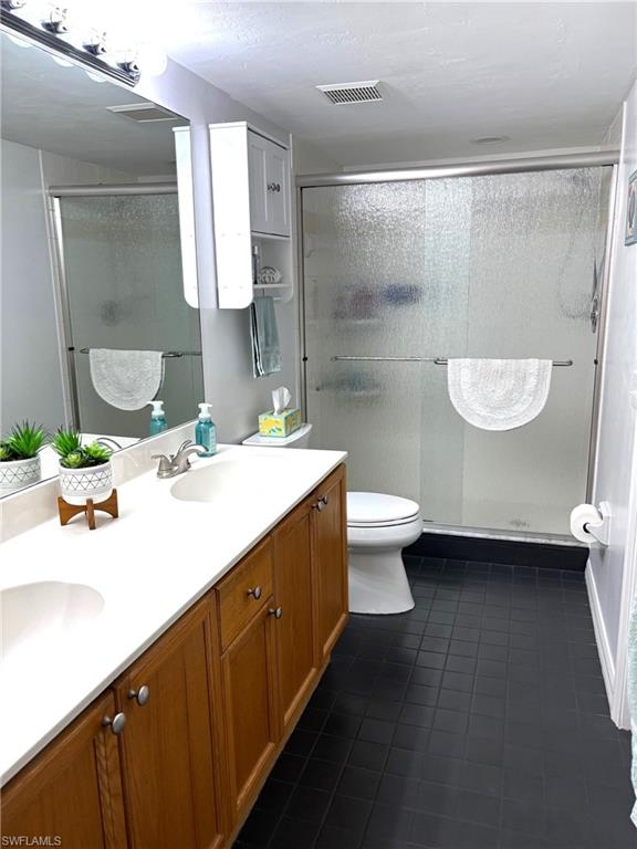 Bathroom featuring toilet, vanity, tile patterned floors, and walk in shower