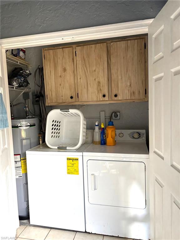 Laundry area with water heater, cabinets, light tile patterned floors, and washing machine and clothes dryer
