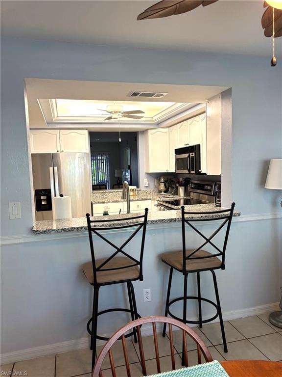 Kitchen featuring kitchen peninsula, appliances with stainless steel finishes, white cabinets, and light tile patterned floors