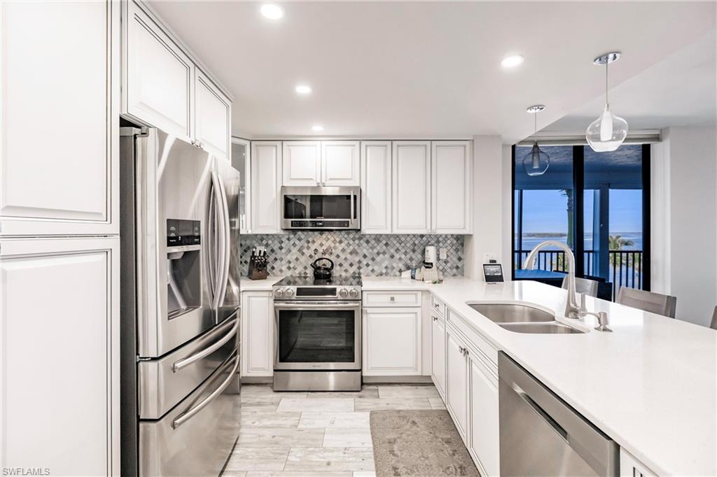 Kitchen with sink, hanging light fixtures, tasteful backsplash, white cabinets, and appliances with stainless steel finishes