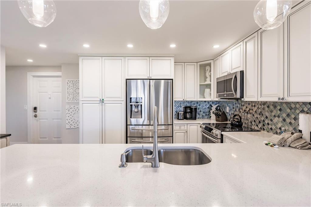 Kitchen with decorative light fixtures, decorative backsplash, white cabinetry, and stainless steel appliances