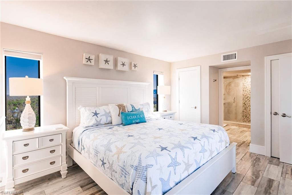 Bedroom with ensuite bath, light hardwood / wood-style floors, and multiple windows