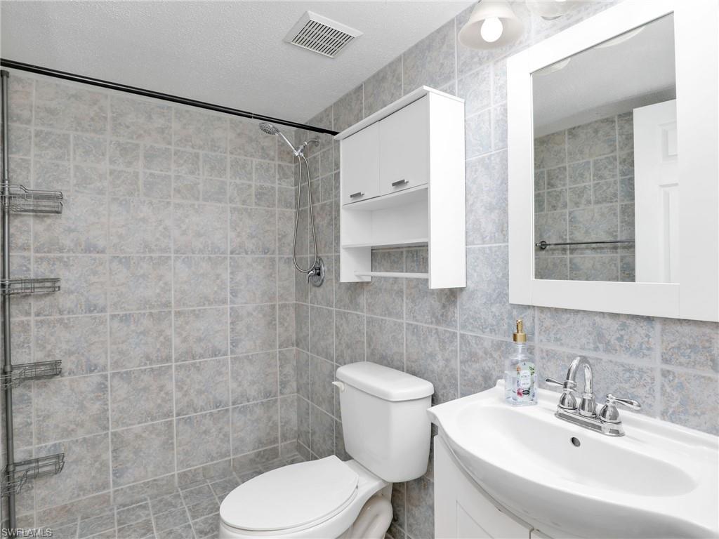 Bathroom featuring tasteful backsplash, vanity, a textured ceiling, tile walls, and toilet