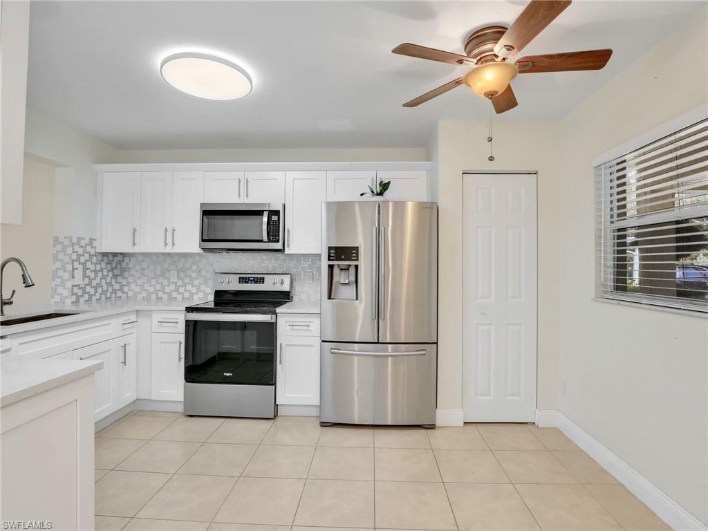 Kitchen with appliances with stainless steel finishes, backsplash, sink, light tile patterned floors, and white cabinetry
