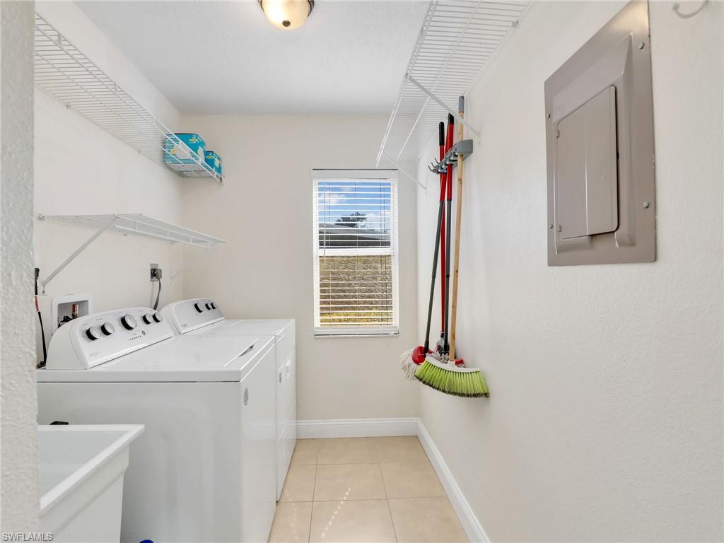 Laundry room featuring light tile patterned floors, electric panel, washer and clothes dryer, and sink