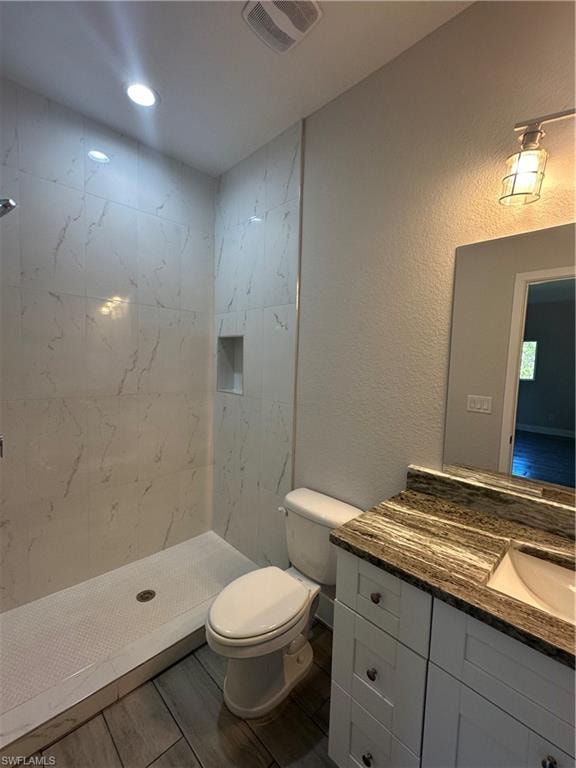 Bathroom featuring a tile shower, vanity, and toilet