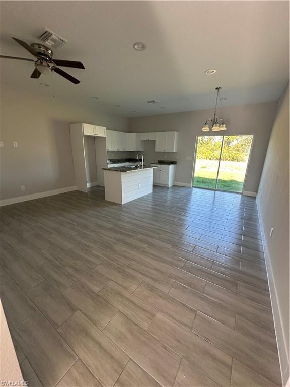 Unfurnished living room with ceiling fan with notable chandelier, light hardwood / wood-style floors, and sink