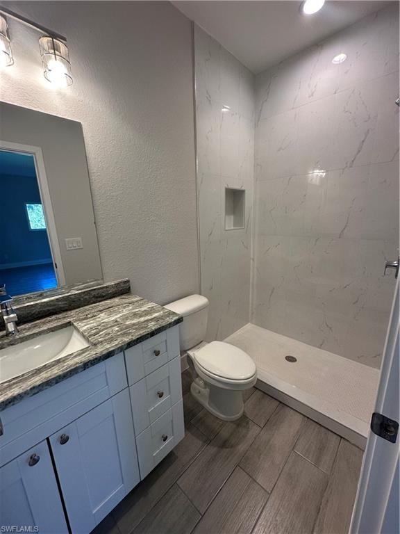 Bathroom featuring a tile shower, vanity, and toilet