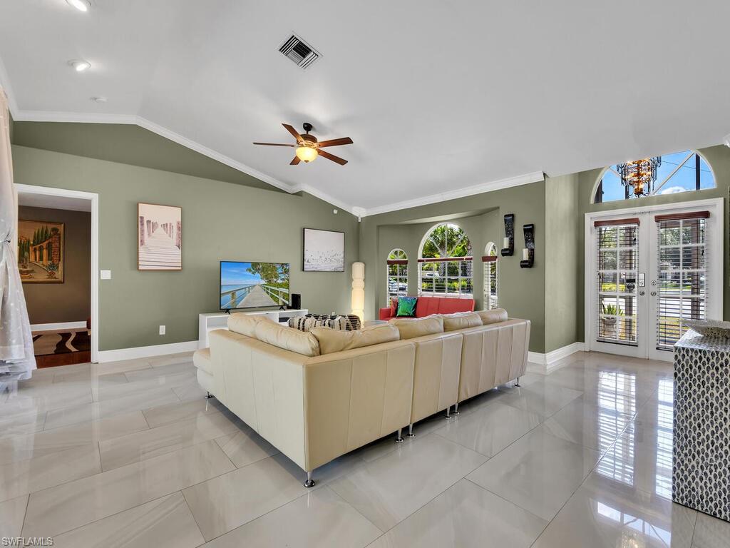 Tiled living room featuring ceiling fan, french doors, crown molding, and vaulted ceiling