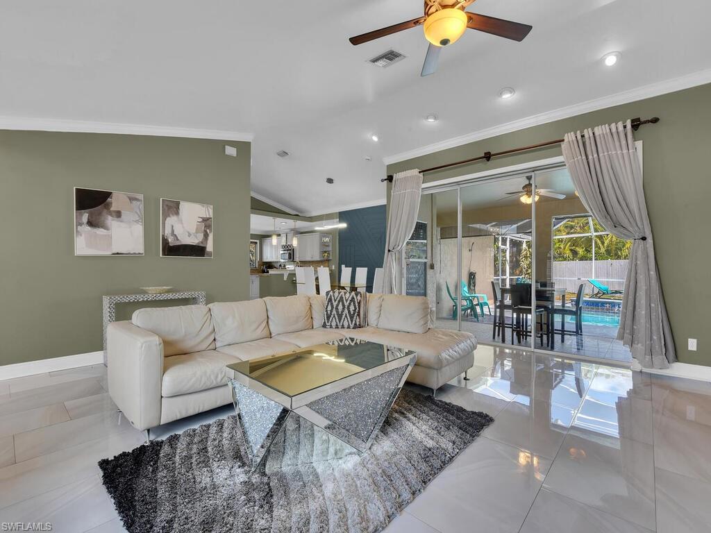 Living room featuring ceiling fan, light tile patterned floors, crown molding, and vaulted ceiling