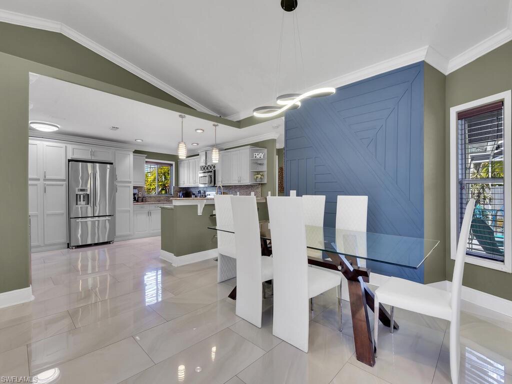 Tiled dining room featuring a healthy amount of sunlight, vaulted ceiling, and ornamental molding