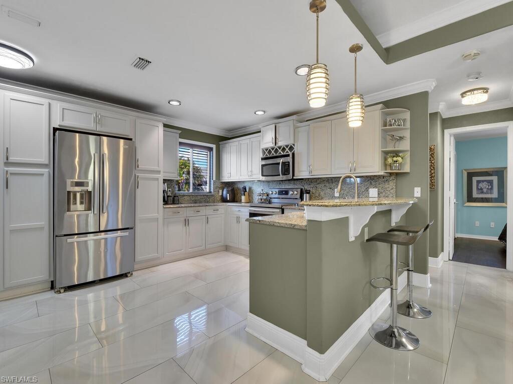 Kitchen featuring backsplash, light stone counters, stainless steel appliances, decorative light fixtures, and white cabinets