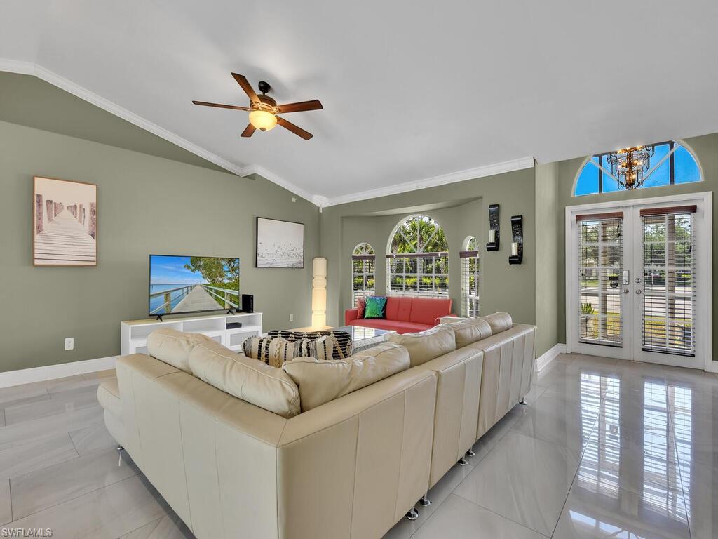 Living room with french doors, ceiling fan with notable chandelier, vaulted ceiling, and crown molding
