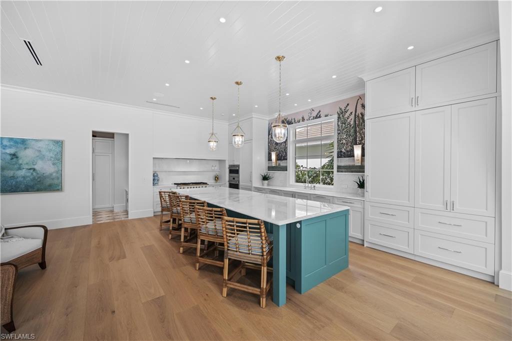 Kitchen featuring a spacious island, light hardwood / wood-style floors, white cabinetry, hanging light fixtures, and a breakfast bar area