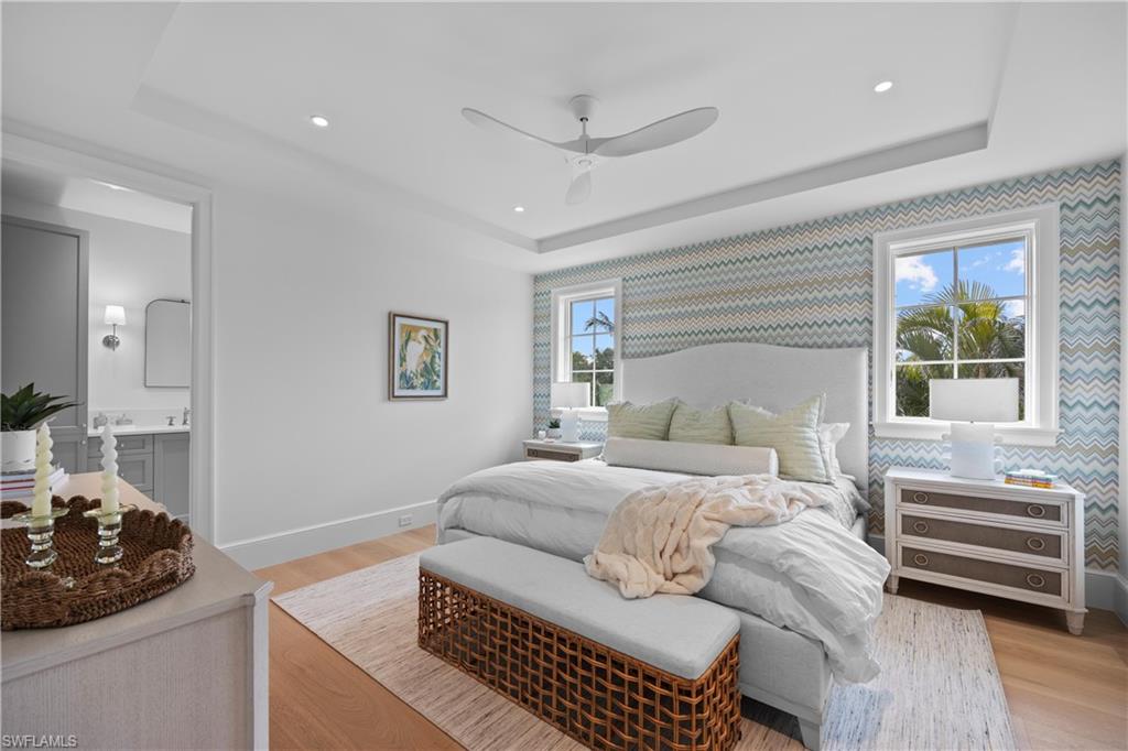 Bedroom featuring light wood-type flooring, ceiling fan, a tray ceiling, and ensuite bath