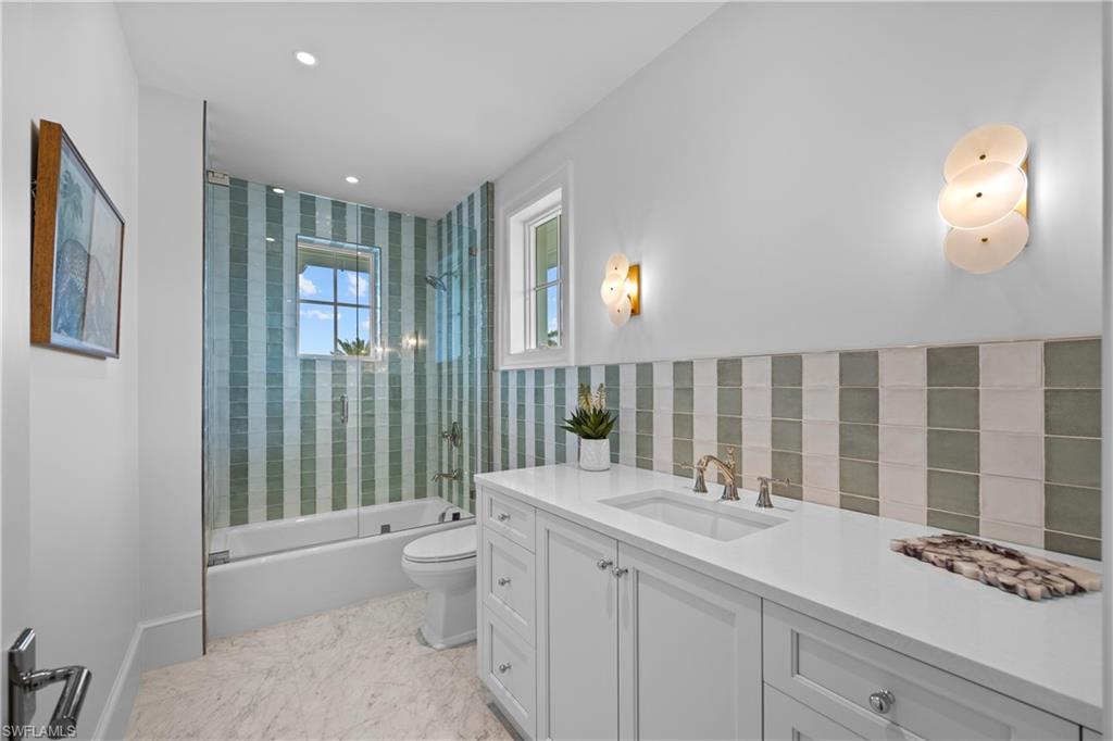 Full bathroom with tile walls, enclosed tub / shower combo, vanity, and toilet