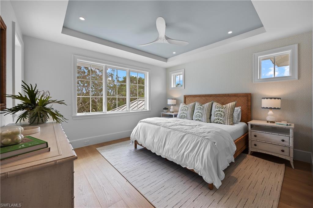 Bedroom with a raised ceiling, ceiling fan, and wood-type flooring