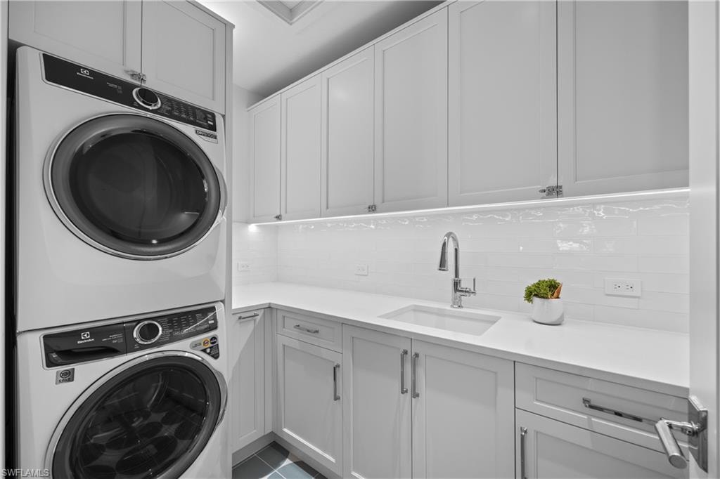 Laundry area with cabinets, sink, light tile patterned floors, and stacked washer and clothes dryer