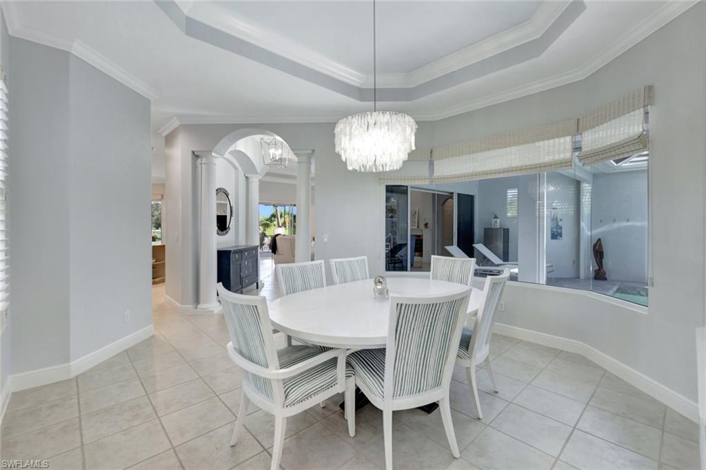 Tiled dining space with decorative columns, crown molding, a tray ceiling, and an inviting chandelier