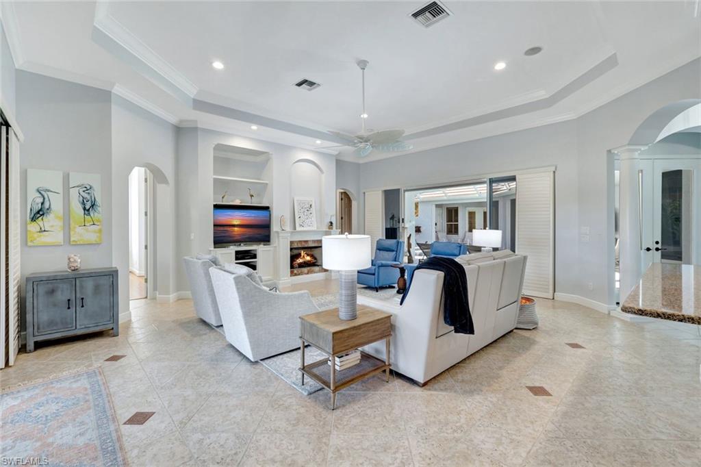 Living room with decorative columns, ornamental molding, built in shelves, a tray ceiling, and ceiling fan