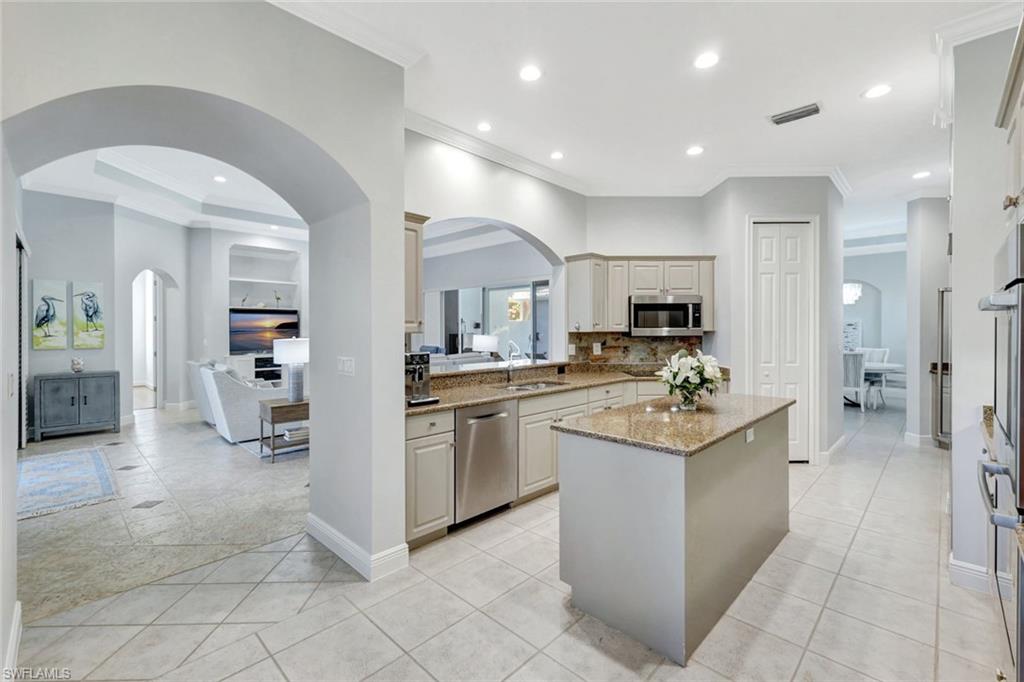Kitchen with appliances with stainless steel finishes, light stone counters, sink, light tile patterned floors, and a center island