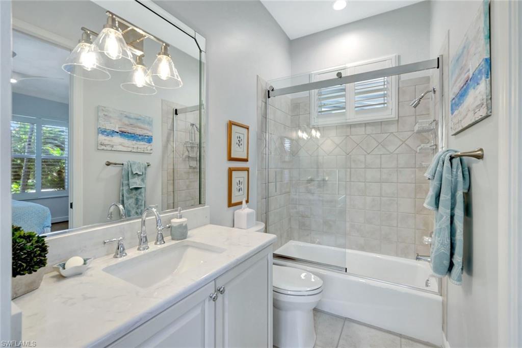 Full bathroom featuring tile patterned flooring, vanity, bath / shower combo with glass door, and toilet, shared hall bath with guest bedroom