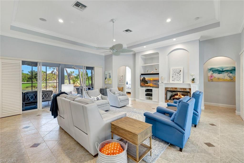 Living room with ornamental molding, a raised ceiling, ceiling fan, light tile patterned floors, and built in features