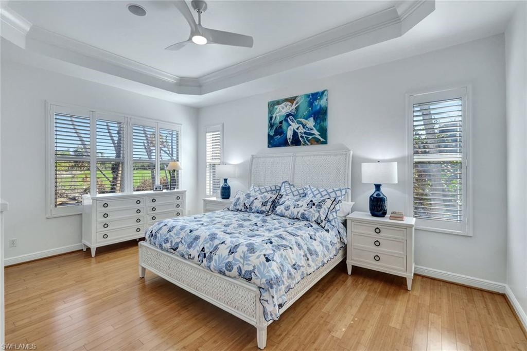Bedroom with light hardwood / wood-style floors, ceiling fan, crown molding, and a tray ceiling